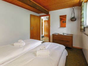Ein Zimmer mit zwei Betten, einem Holzschrank, einem Spiegel und einer hängenden Pflanze.