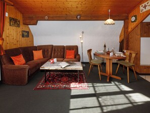 A cozy living room with a brown sofa, a dining table with chairs, a patterned rug, and a wooden ceiling. - Strassscheuer by Interhome (Grindelwald)