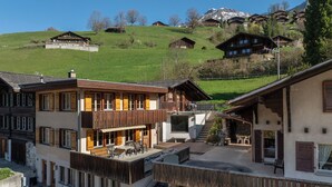 Ein mehrstöckiges Hotel mit Balkon, Außenbereich und Blick auf einen grünen Hügel mit weiteren Gebäuden.