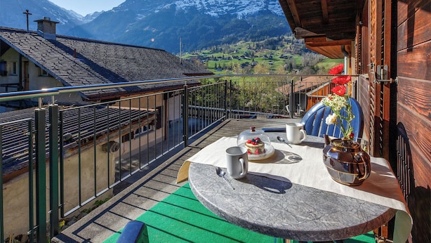 Ein Balkon mit Tisch, Stühlen und Blick auf schneebedeckte Berge.