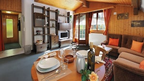 Ein gemütliches Zimmer mit Esstisch für zwei Personen, einer Couch, einem Fernseher und einer Holzwand mit Regalen.