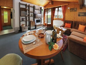 Ein gemütliches Zimmer mit Esstisch für zwei Personen, einer Couch, einem Fernseher und einer Holzwand mit Regalen.
