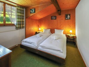 A double bed with white linens, two bedside tables with lamps, wooden walls, and a window with curtains. - Strassscheuer by Interhome (Grindelwald)