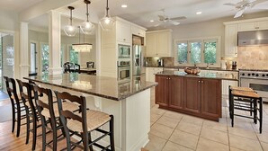Une cuisine spacieuse avec un grand îlot central, des chaises en bois et un ventilateur de plafond.