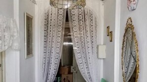 Un pasillo estrecho con un techo decorativo, una silla verde, una mesa con figuritas y un espejo en la pared.