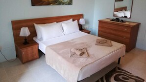 Una cama bien hecha con sábanas blancas, un cabecero de madera, una lámpara de noche, un tocador de madera, un espejo y un adorno de pared.