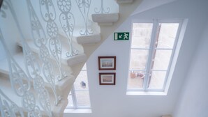 Una escalera con barandales blancos ornamentales y una barandilla de madera, que conduce a un rellano con un pequeño ventanal y cuadros enmarcados.