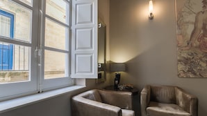 A room with two leather armchairs, a table with a lamp, a large mirror, and a window with open shutters. - JM - Casa Rooms (Valletta)