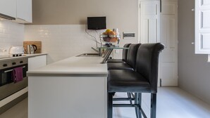 A modern kitchen with white cabinets, a stainless steel kettle, a toaster, and a glass coffee table. - JM - Casa Rooms (Valletta)