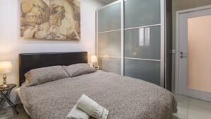 A bedroom with a large bed, a sliding glass door, a painting on the wall, and a nightstand with lamps. - JM - Casa Rooms (Valletta)