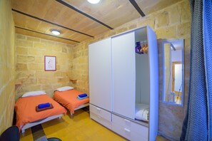 Ein Schlafzimmer mit zwei Betten, einem Kleiderschrank, einem Spiegel und einer Steinwand.