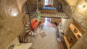 Ein Zimmer mit Steinwänden, einer Wendeltreppe, einem Bett und einem kleinen Tisch mit einem Ventilator.