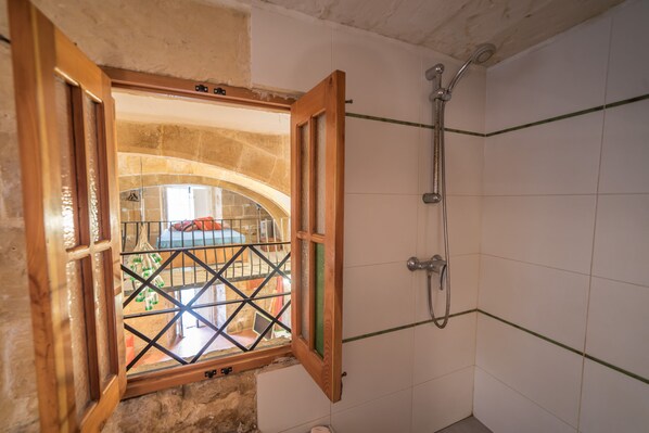 A bathroom with a shower, a window with a wooden frame, and a view of an outdoor area.