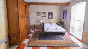Un dormitori amb llit, armari de fusta, parets de pedra i terra quadriculada.