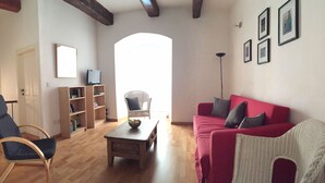 Ein Wohnzimmer mit einem roten Sofa, einem Holztisch, einem Korbstuhl, einem Bücherregal und einem Fernseher.