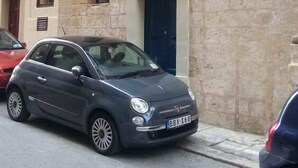 Ein zweistöckiges Gebäude mit einem blauen Balkon und einem geparkten Auto davor.