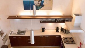 Eine kompakte Küche mit Essbereich, ausgestattet mit einem Holztisch und -stühlen, einer hängenden Leuchte sowie einem Gemälde mit Meeresblick über der Arbeitsfläche.