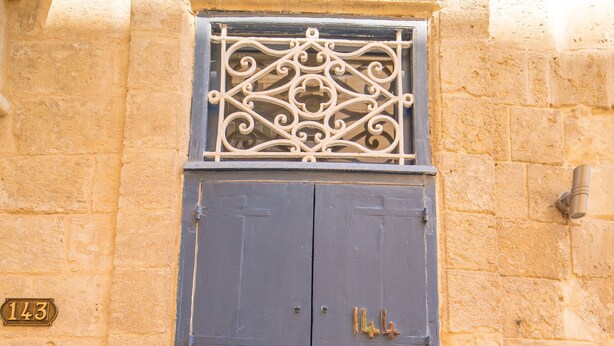 A dark blue door with two lion head knockers, a decorative metal grille above, and a number plaque. - TA - Casa Rooms (Valletta)