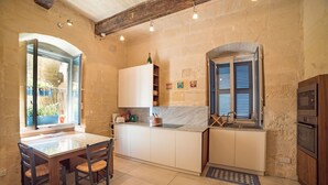 A kitchen with a marble countertop, wooden chairs, a built-in oven, and a window with blue shutters. - TA - Casa Rooms (Valletta)