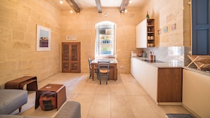 A compact kitchen with a dining area, stone walls, wooden beams, and a window with a view. - TA - Casa Rooms (Valletta)