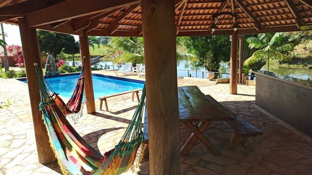 Un espacio al aire libre techado con piscina, bancos de madera y una hamaca.