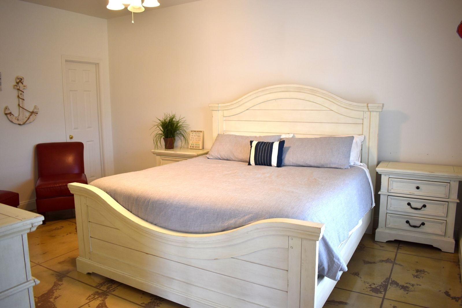 Ein Schlafzimmer mit einem weißen Bett, einem roten Sessel, einem Nachttisch und einer an der Wand befestigten Pflanze.