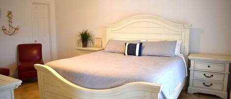 Ein Schlafzimmer mit einem weißen Bett, einem roten Sessel, einem Nachttisch und einer an der Wand befestigten Pflanze.