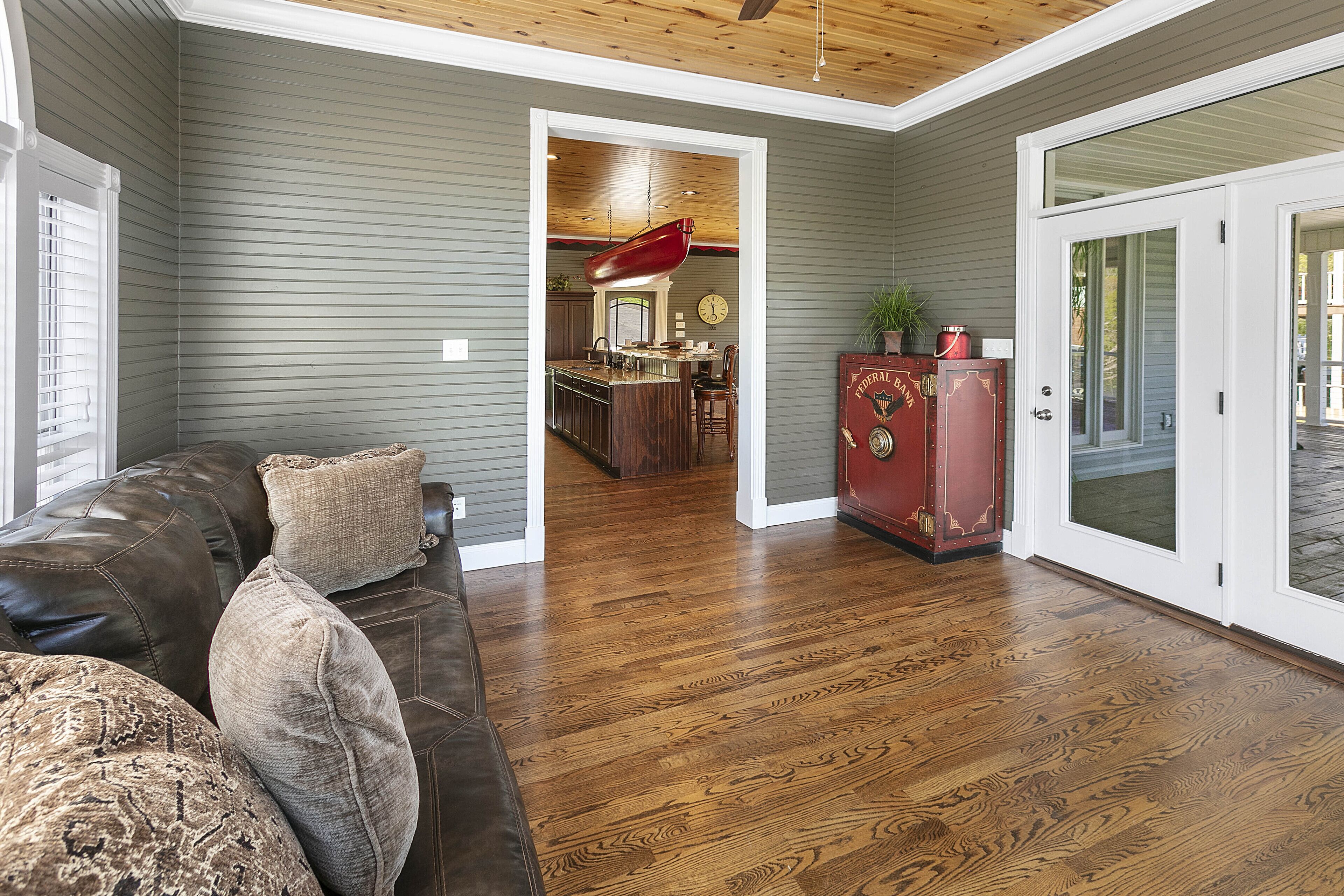 A living room with a brown leather sofa, a wooden floor, and a kitchen in the background.