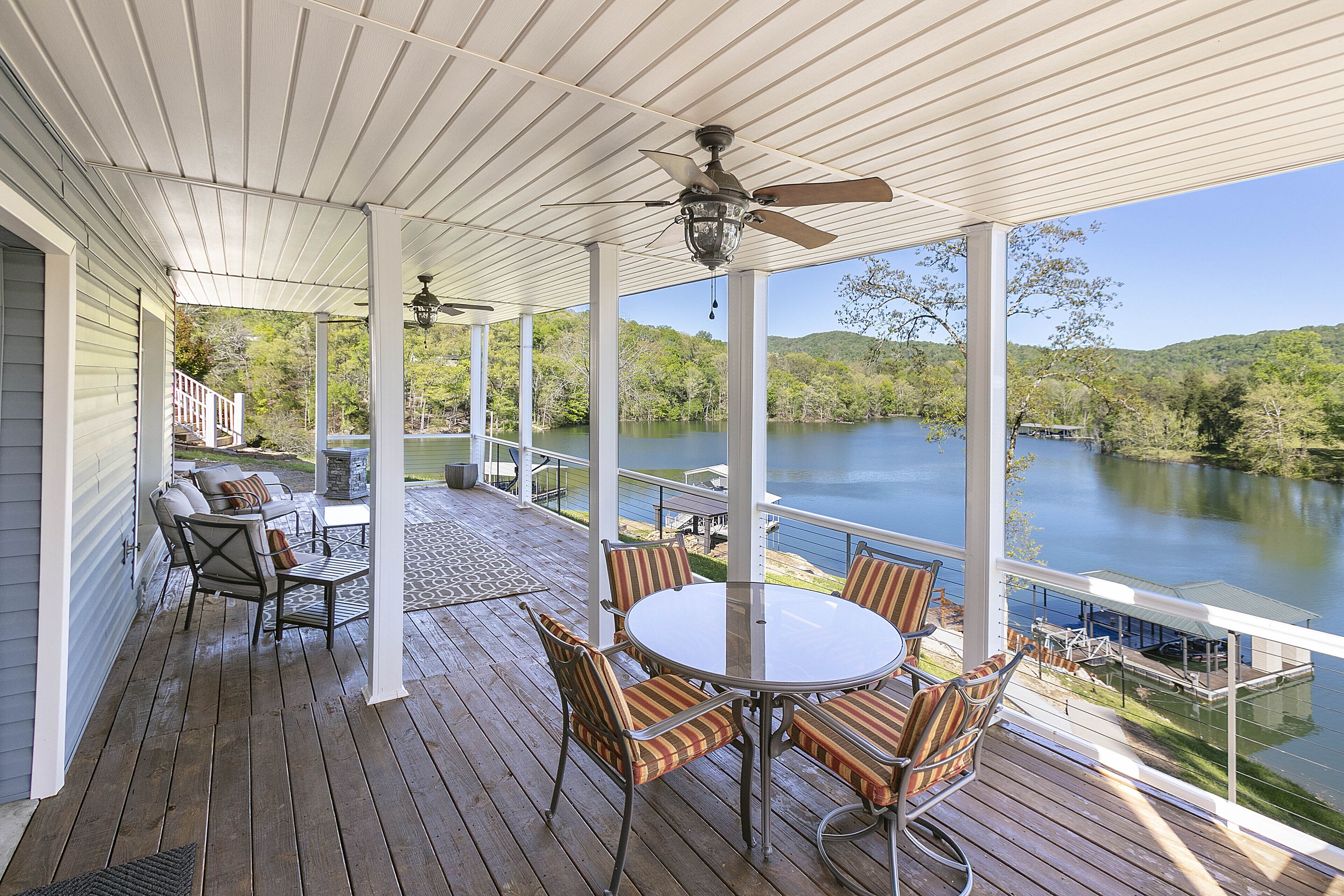A covered deck with a table and chairs, overlooking a lake.
