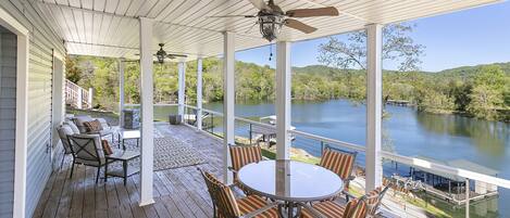 A covered deck with a table and chairs, overlooking a lake.