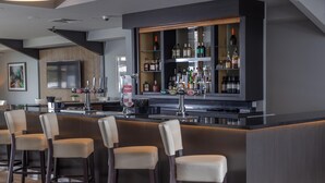 A modern bar area with a counter, bar stools, and a variety of liquor bottles. - Cambridge Bar Hill Hotel, BW Signature Collection (Cambridge)