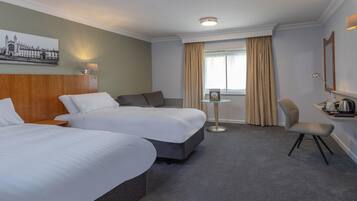 Une chambre d’hôtel avec deux lits, une petite table, une chaise, une lampe et un tableau au mur.