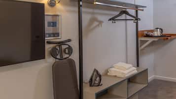 Et hotelværelse med seng, fjernsyn, spejl, håndklædestativ og et hyldesæt med toiletartikler.
