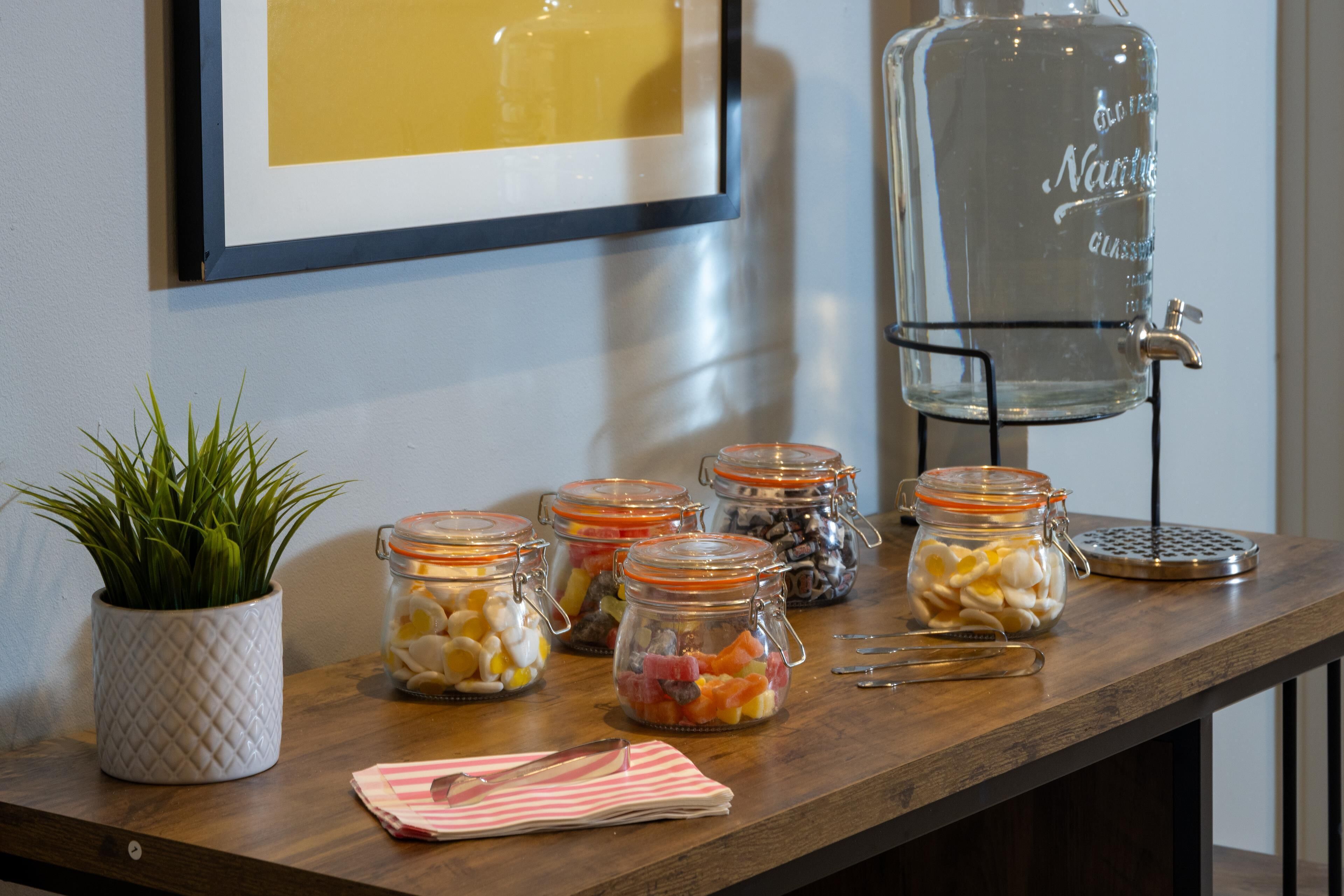A wooden table with glass jars containing various snacks, a potted plant, and a water dispenser.