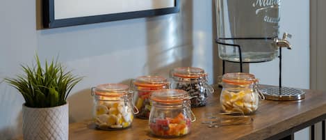 A wooden table with glass jars containing various snacks, a potted plant, and a water dispenser.