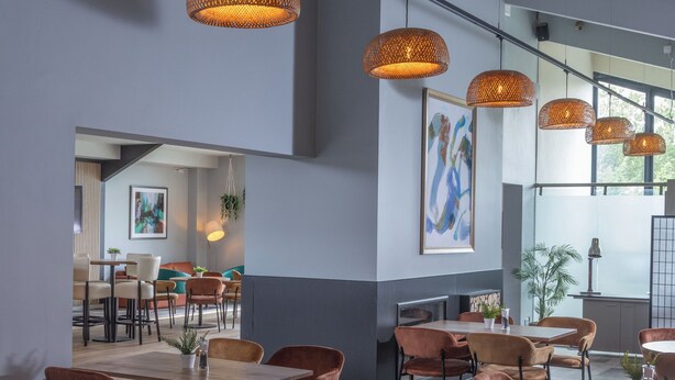 A modern dining area with wooden tables and brown chairs, featuring pendant lighting and a large window providing natural light. - Cambridge Bar Hill Hotel, BW Signature Collection (Cambridge)
