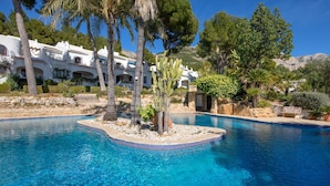A clear blue pool with a small island in the center, surrounded by palm trees and cacti. - Cosy apartment for 3 people with pool, WIFI, TV and terrace (Denia)