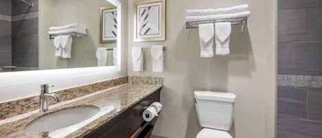 A bathroom with a granite countertop sink, a toilet, and towels hanging on a rack.