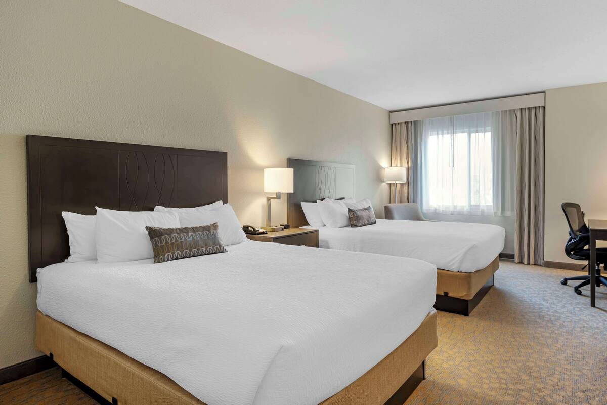 A hotel room with two beds, a desk, and a chair.