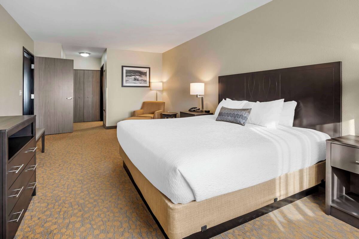 A hotel room with a large bed, a desk, a chair, a wardrobe, and a nightstand with a lamp.