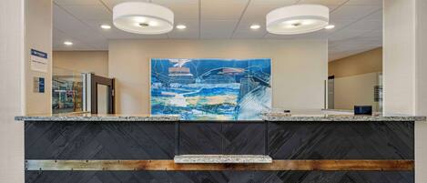A reception area with a modern design, featuring a large abstract painting on the wall, a herringbone-patterned counter, and recessed lighting.
