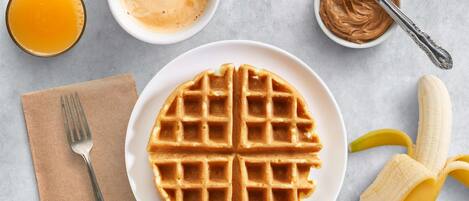 A plate of waffles, a banana, a glass of orange juice, a bowl of peanut butter, and a cup of coffee on a table.