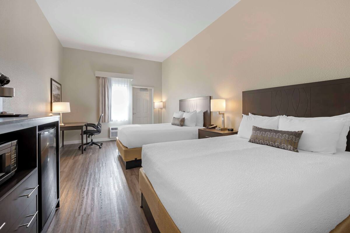 A hotel room with two beds, a desk with a lamp, a chair, and a microwave.