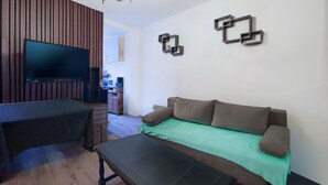 A modern living room with a flat-screen TV, a sofa with a green blanket, a coffee table, and a wooden accent wall. - T2, 48 M2 near the spa (Aix les Bains)