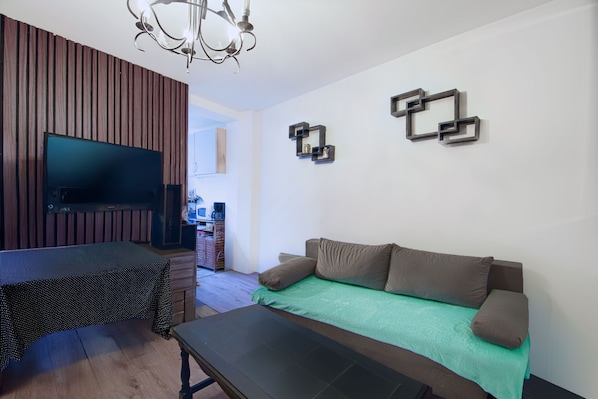 Un salon moderne avec un téléviseur à écran plat, un canapé recouvert d’un plaid vert, une table basse et un mur décoratif en bois.