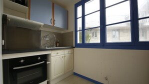 A kitchen with white cabinets, a black oven, a window with blue trim, and a view of a building outside. - T2, 48 M2 near the spa (Aix les Bains)