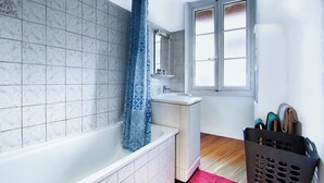 A bathroom with a bathtub, a sink, a window, and a laundry basket. - T2, 48 M2 near the spa (Aix les Bains)
