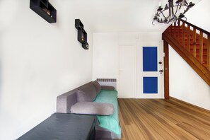 Une pièce avec un plancher en bois, un canapé, une petite table, une étagère fixée au mur et un escalier.