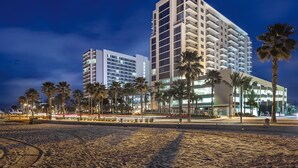 Un hôtel en bord de mer, avec plusieurs étages, des palmiers et une plage de sable.