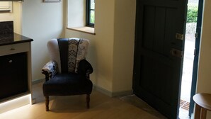 A room with a dark wooden door, a chair with a patterned cushion, a small window, and a ceiling light fixture.